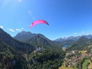 Pinker Tandem Gleitschirm fliegt bei blauem Himmel über Schloss Neuschwanstein